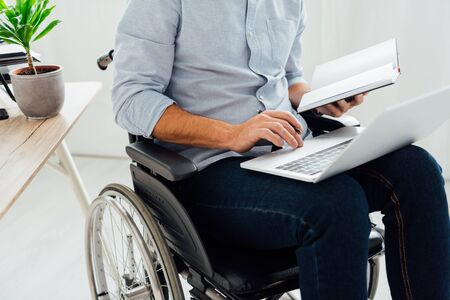 Cropped view of man in wheelchair holding notebook and laptopの写真素材