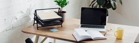 Notebook, laptop with blank screen and cup on working table, panoramic shotの写真素材
