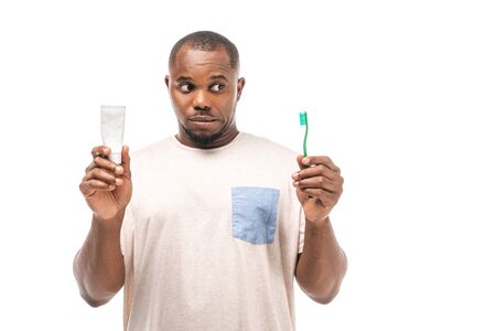 skeptical african american man holding toothbrush and toothpaste isolated on whiteの写真素材