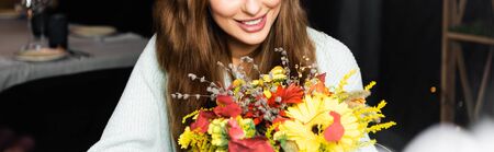 cropped view of happy woman with bouquet of autumn flowers in cafe