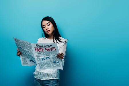 asian woman in white blouse reading newspaper with fake news on blue backgroundの写真素材