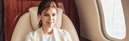 panoramic shot of attractive businesswoman smiling in private plane