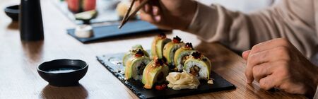 panoramic shot of man holding chopsticks near plate with sushiの写真素材