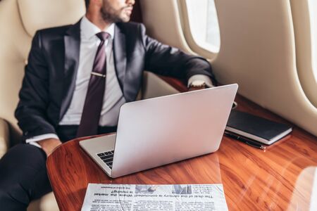 cropped view of businessman in suit and laptop on table in private planeの写真素材
