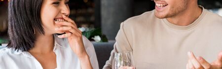 panoramic shot of happy man gesturing near woman laughing in restaurantの写真素材