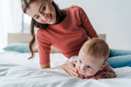 selective focus cute infant baby near beautiful mother in bedroomの写真素材