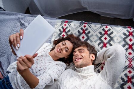 high angle view of attractive girlfriend and smiling boyfriend in sweater looking at digital tablet