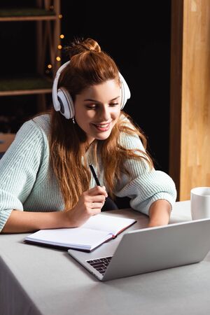 smiling woman in headphones watching webinar on laptop in cafe