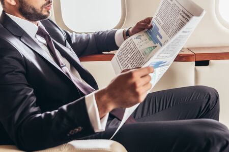 cropped view of businessman in suit reading newspaper in private plane