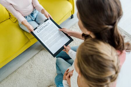 overhead view of mother standing with daughter and giving clipboard to babysitter
