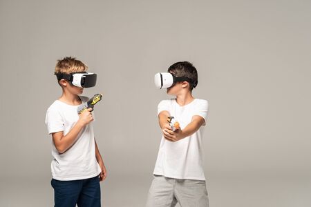 two brothers in vr headsets looking at each other while holding toy guns isolated on greyの写真素材