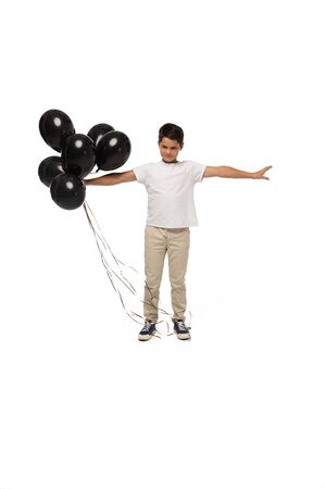 serious boy standing with outstretched hands while holding black balloons on white backgroundの写真素材