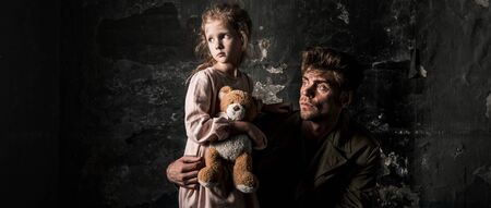 panoramic shot of upset man near kid with teddy bear in dirty room, post apocalyptic conceptの写真素材