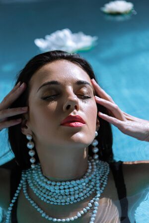 attractive woman in pearl necklace posing with closed eyes in poolの写真素材