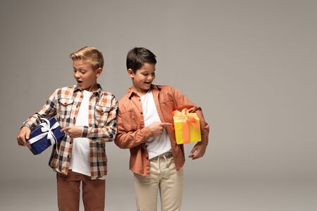 surprised brothers pointing with fingers at blue and yellow gift boxes isolated on greyの写真素材