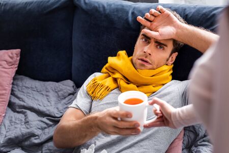 cropped view of girlfriend giving cup of tea to sick boyfriendの写真素材