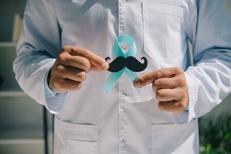partial view of doctor holding blue awareness ribbon and paper cut mustacheの写真素材