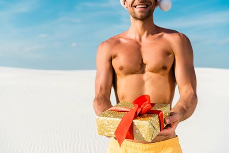 cropped view of sexy man in santa hat holding gift on beach in Maldivesの写真素材