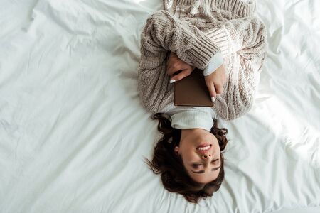 top view of smiling woman in sweater lying in bed at morningの写真素材