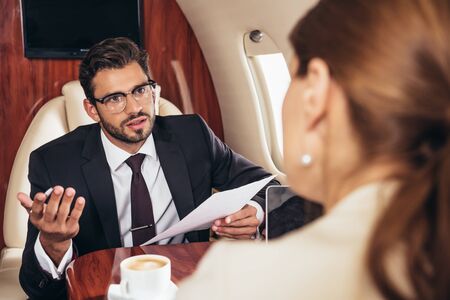 selective focus of businessman looking at businesswoman and holding paper in private planeの写真素材
