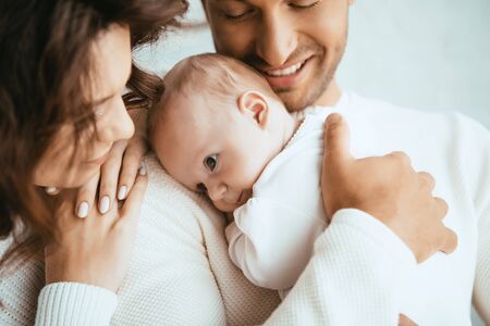 cropped view of happy man holding adorable baby near smiling wifeの写真素材