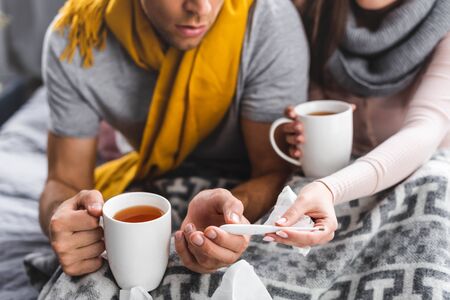 cropped view of sick girlfriend and boyfriend holding cups and thermometerの写真素材