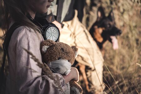 cropped view kid with gas mask holding teddy bear near man and dog, post apocalyptic conceptの写真素材