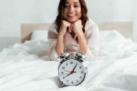 selective focus of attractive woman looking at alarm clock at morningの写真素材
