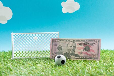 toy soccer ball and gates near dollar banknote on blue background with clouds, sports betting conceptの写真素材
