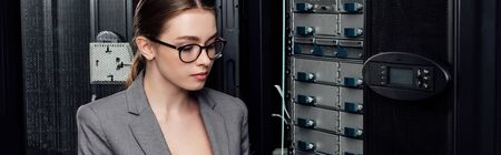 panoramic shot of attractive businesswoman in glasses near server rack in data centerの写真素材