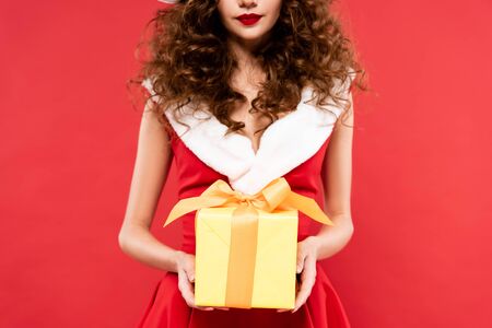 cropped view of girl in santa costume holding christmas gift, isolated on redの写真素材
