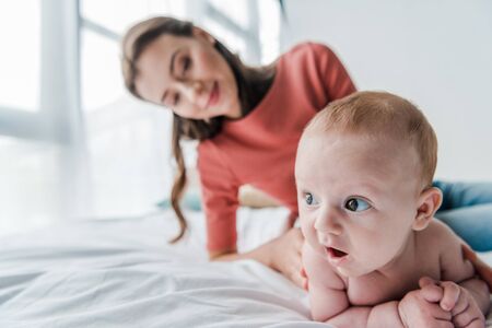 selective focus cute infant baby near happy mother in bedroomの写真素材