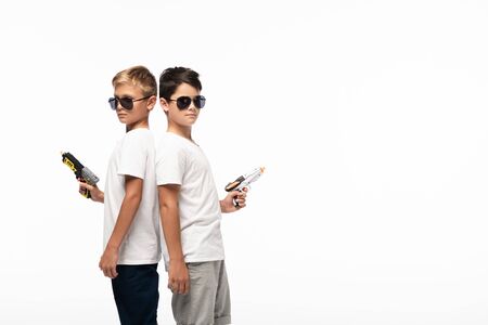 two brothers in sunglasses standing back to back and holding toy guns while playing gangsters...