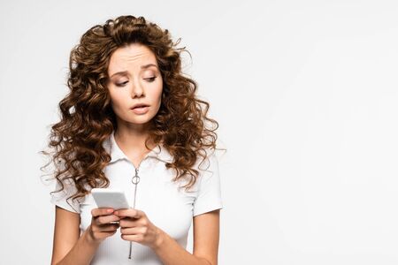 thoughtful curly girl using smartphone, isolated on whiteの写真素材