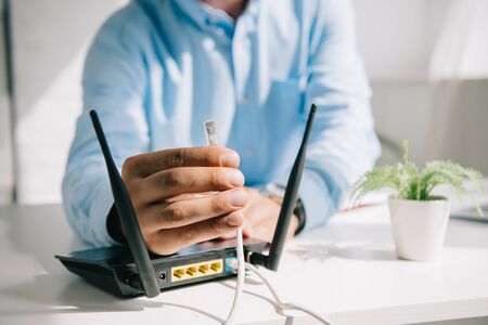 selective focus of businessman holding wire with connector near routerの写真素材