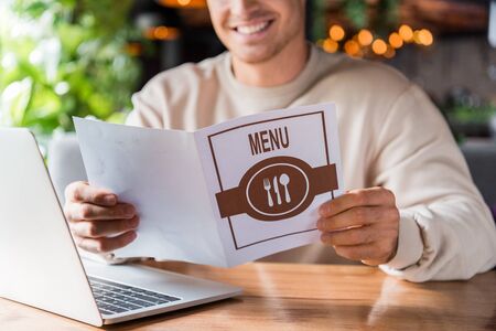 cropped view of happy man holding menu near laptop in restaurantの写真素材