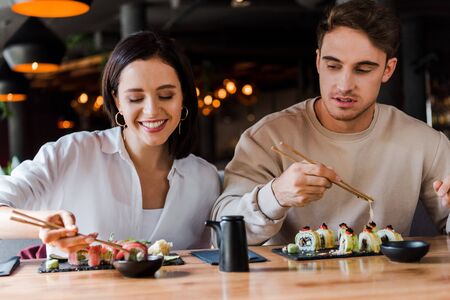 selective focus of young man holding chopsticks near happy woman in sushi barの写真素材