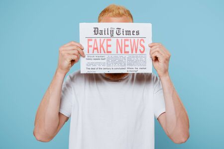 man holding newspaper with fake news in front of face, isolated on blueの写真素材