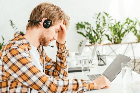 tired bearded broker touching head while sitting near laptop