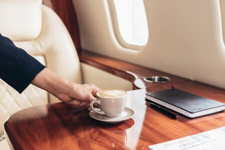 cropped view of flight attendant putting cup of coffee on table in private planeの写真素材