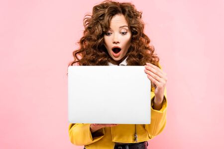 beautiful shocked curly woman using laptop, isolated on pinkの写真素材