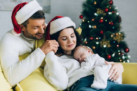 happy man touching hand of smiling wife holding sleeping babyの写真素材