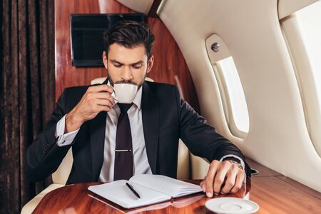 handsome businessman in suit drinking coffee in private plane
