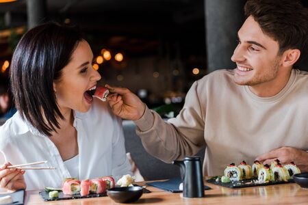 selective focus of happy man holding chopsticks with tasty sushi near young woman in restaurantの写真素材