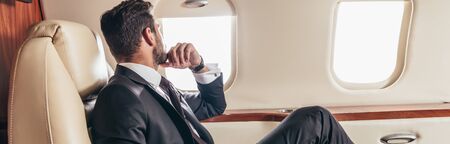 panoramic shot of businessman in suit looking through window in private planeの写真素材
