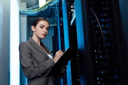 beautiful businesswoman writing while holding clipboard in server roomの写真素材