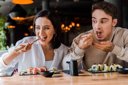 young man and woman eating tasty sushi in sushi barの写真素材