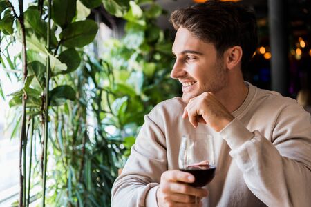 happy man holding glass with red wine in restaurantの写真素材