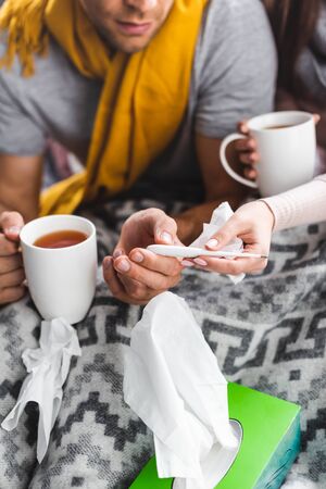 cropped view of sick girlfriend and boyfriend holding cups and thermometerの写真素材