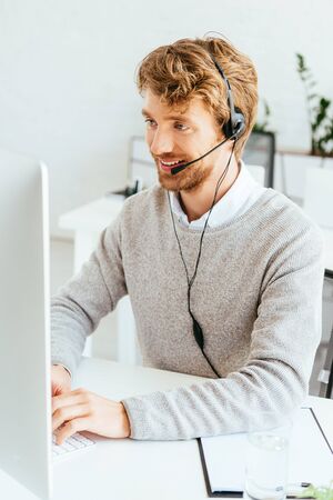 happy bearded operator in brokers agency in headset typing on computer keyboard